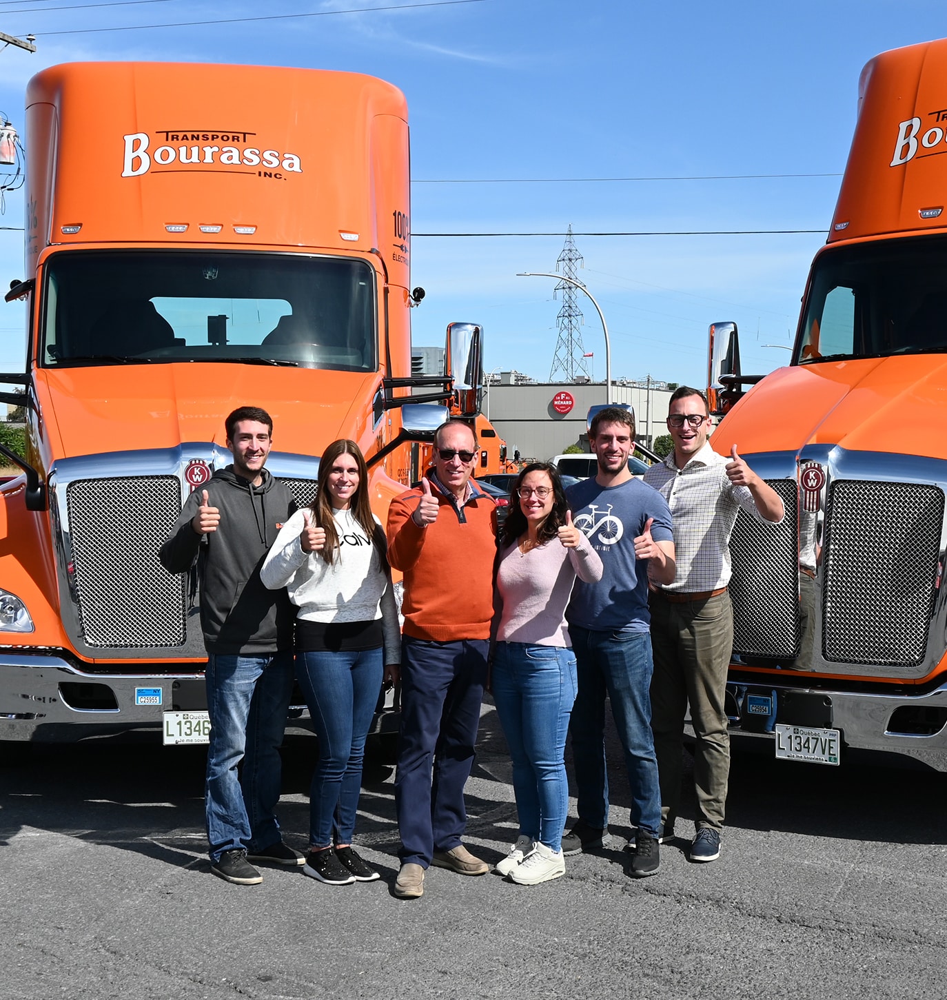 Employés de Transport Bourassa posant devant deux cabines de camion, souriants et faisant des thumbs-up.