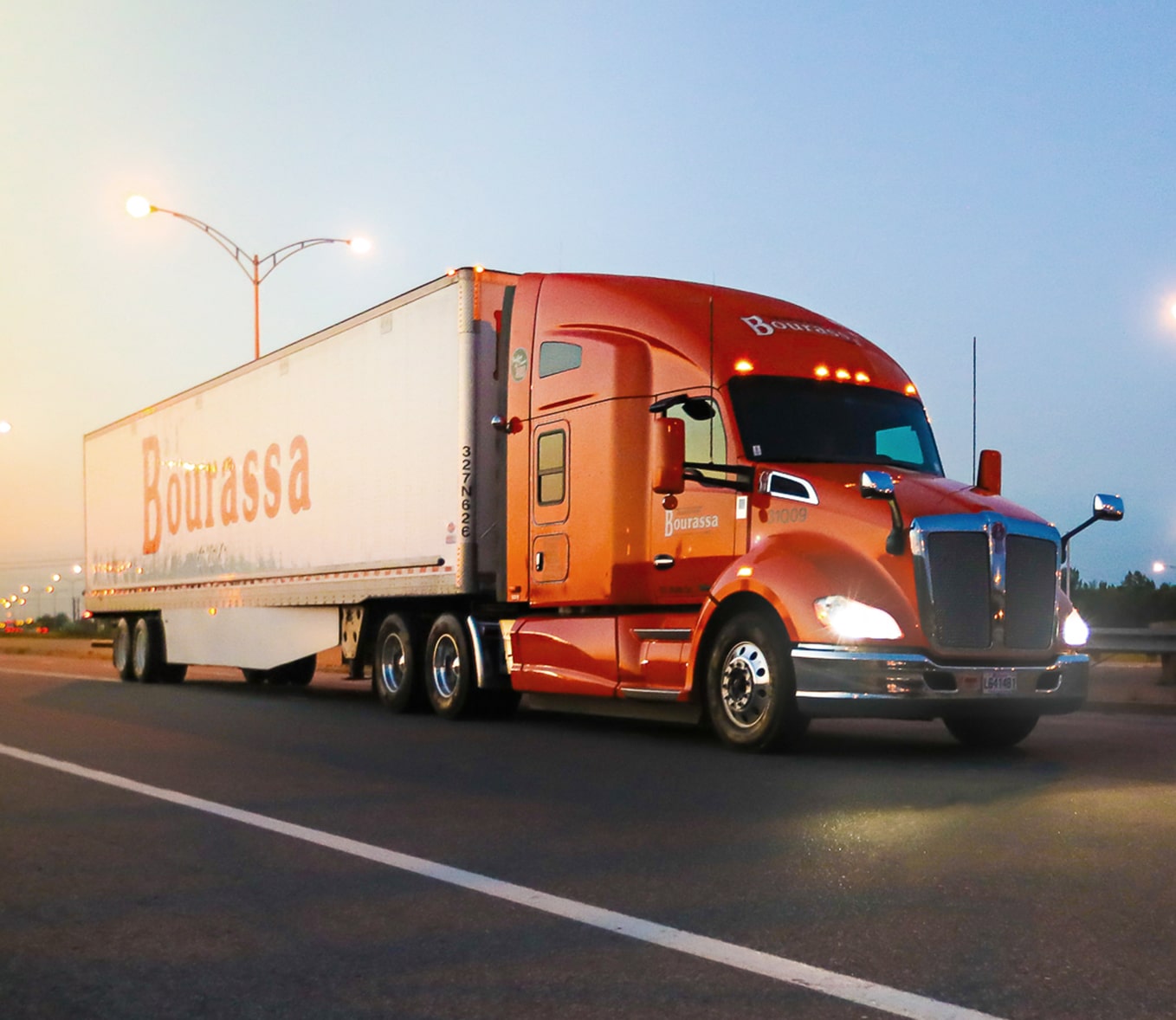 Un camion remorque Transport Bourassa circule sur l'autoroute à l'aube.